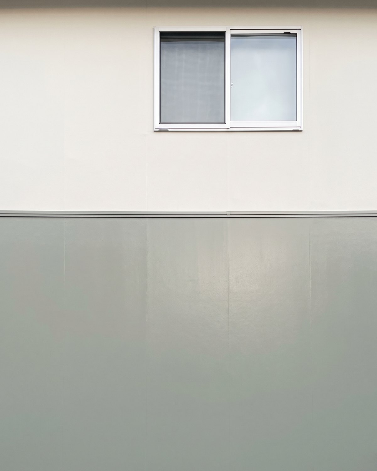 艶を抑えた白と、艶のある灰緑が、水切りの線でまっすぐ塗り分けられた外壁